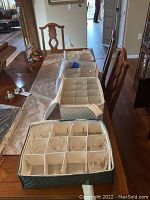 Three fabric-lined boxes with dividers holding assorted glassware and packing material on dining table