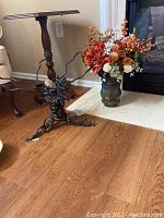 Photo showing wrought iron stand with twisted branches and hand painted metal vase with faux flowers placed nearby.