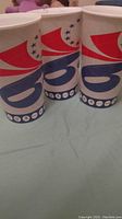 Three paper cups with Philadelphia 76ers logo and design in red, white, and blue with 13 blue stars.