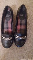 Pair of black dress shoes with chain detail on the front, seen from top view showing interior plaid lining and brand Hot Kiss.