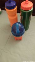 Four plastic bottles on light green fabric surface: two tall sports bottles, one small bottle with dome lid and straw