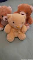 Front view of three small vintage teddy bears: two light brown with cream accents and one pale yellow with ribbon bow.