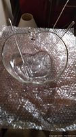 Top view of the clear glass salad bowl with serving fork and spoon resting inside on bubble wrap.