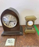 Two mantle clocks side by side on a wooden surface. Left is a dark wooden Seth Thomas clock, right is a smaller gilt bronze French clock with four columns.