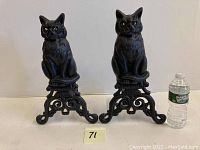 Pair of cast iron figural cat andirons displayed side by side with water bottle for scale