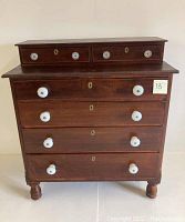 Front view of antique wooden dresser showing all drawers with opalescent glass knobs.