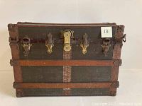 Full view of antique steamer trunk with metal and wood reinforcements, showing front face with central lock and side latches.