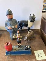 Shows all items together: the cast iron banks, Boston Terrier door stop, and cardboard police officer figure.