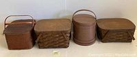 Photo of three picnic baskets and one wooden firkin bucket aligned side by side on a floor against a wall.