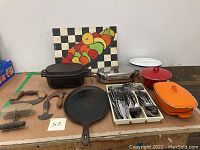 Full overview of the lot showing enamel pots, cast iron skillets, flatware tray, kitchen tools and small painting.