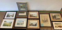 Overview of the ten framed watercolor paintings arranged on the floor showing diverse landscape and nautical scenes, varying frame styles and colors.