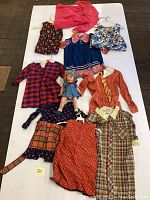 Overview of lot with Shirley Temple doll and eight pieces of vintage girls' clothing in various patterns and colors.