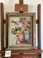 Framed vintage oil painting of flowers in vase on wooden easel.