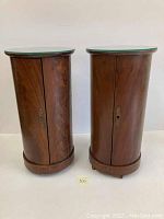 Front view of two vintage tall drum-shaped wooden cabinets with glass tops placed side by side.