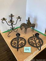 Full view of Don Quixote statue on horse with two round wrought iron tree of life wall sconces and one wrought iron three-arm candelabra on flat surface.