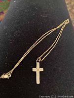 Full view of the gold box chain with cross pendant laid out on black fabric, showing chain and charm length and style.