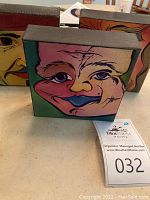 Three colorful small canvas acrylic paintings depicting whimsical faces showing distinct expressions and styles, displayed together on a table.