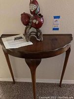 Full view of the half circle accent table with ceramic sculpture on top, showing scalloped edges and wooden finish.