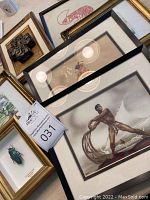 Various small framed art prints and paper cuts including a framed glass bug sculpture and carved lobster image, arrayed together on a surface.