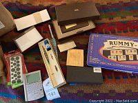 Photo showing Rummy-O game metal tin, fountain pen in box with ink bottle, Franklin electronic dictionary, assorted stationery including sticky dots, and some paper pads.