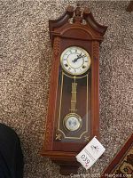 Front view of wooden wall clock showing face, pendulum, and carved details