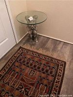 Full view of gargoyle base table with round glass top next to decorative area rug.