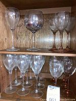 Multiple shelves of assorted glassware including tall wine glasses and snifter alongside others with faint amber tint.