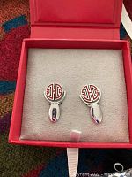 Pair of silver-tone cufflinks with red and white monogram design in a red box