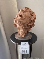 Front angled view of the ceramic head sculpture showing facial features and hair texture on the metal pedestal with auction tag.