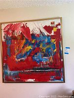 Framed large abstract painting with red, blue, yellow, and white brush strokes on wall with a blue auction sticker to the right.