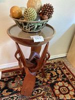Overall view of the wooden bowl set on the carved wooden stand, showing the interlocking design and glass insert tabletop, as well as glass bowl with decorative orbs on top.