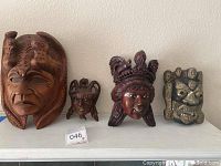 Full frontal shot of four wooden ethnic masks arranged left to right by size on a white surface with mounting frames visible at the back.