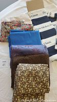 Fabric pieces including white lace, a multicolored floral pattern, solid royal blue, purple with floral pattern, brown textured, and brown floral fabric.