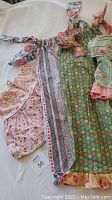 Clothing items laid out on a white surface showing green floral dress with ruffled hem, pink and white floral garment, and blue floral clothing.
