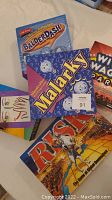 Top view of Malarky, Balderdash, Risk, Wild Wacky Party Game, and a colorful drawing pad on a surface.