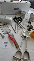 Overview photo showing the entire assortment of Williams Sonoma kitchen tools including creamer, sugar bowl, butter dish, meat tenderizer, salad tongs, ladles, knives and peelers, along with aluminum case and small yellow bowl.