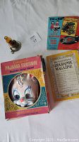 Top view showing colorful clown mask in original Colgusville pajama costume box, small mini oil lamp, children's Read and Hear Golden Book with record, and 1946 National Geographic Magazine.