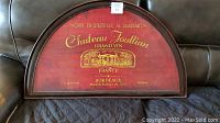 Overall photo of the half barrel shaped metal wall décor with Chateau Joullian Bordeaux Grand Vin wording and French imagery on red background.