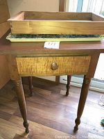 Wooden accent table with small drawer showing dovetail joints and turned legs, measuring approximately 20 x 19.5 x 29 inches. Bamboo tray and laminated plastic cat motif tray stacked on top.