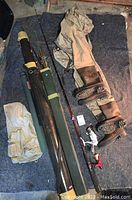 Photo showing fishing poles, green and black rod tube cases, tan fishing vest, and two pairs of brown and tan Cabela's waders with boots attached.