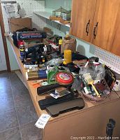 View of table laden with assorted tools, repair supplies, cardboard boxes, and cabinetry in background