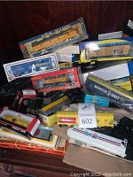 Various HO scale model trains and freight cars in original boxes and loose, displayed on wooden surface with visible brand logos and model names.