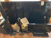 Photo showing all components together: the 65-inch LG TV positioned upright with Panasonic home theater components including tower speakers, smaller speakers, and base unit arranged in front, cables and manuals scattered on the floor.