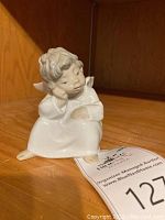 Front and side views of the white porcelain figurine showing the cherub seated with one hand supporting its head.