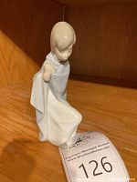 Porcelain figurine of a shepherd boy on a wooden shelf with auction tag number 126 in front. Figurine is approx 6 inches tall and in good visible condition, missing the staff.