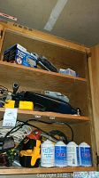 Wooden cabinet shelf with blue and black electric tool, yellow toolbox, power cords, and various hand tools.