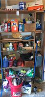 Full view of wooden shelving unit with assorted garage supplies including paint, automotive fluids, cleaning products, tools, and household items.