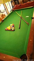 Full view of green-felt pool table with wooden frame, two cues crossed and racked balls on table