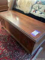 Front and side view of wooden rolling chest showing carved panels, scratches on top, and warm brown finish.