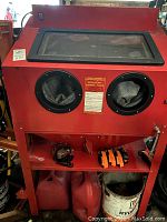 Front view of red sandblasting cabinet showing viewing window, glove ports and shelf with straps